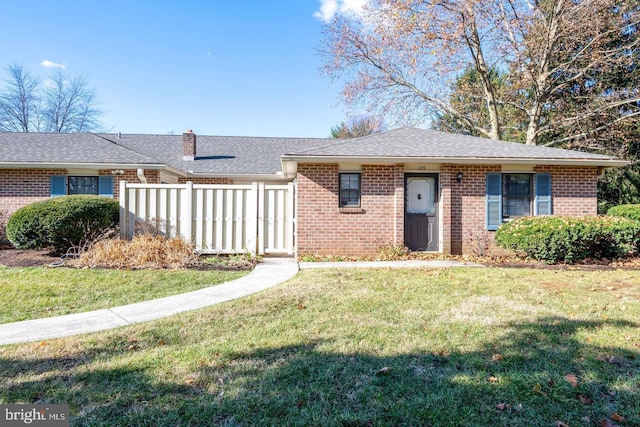 view of front of house featuring brick siding, roof with shingles, a front yard, and fence