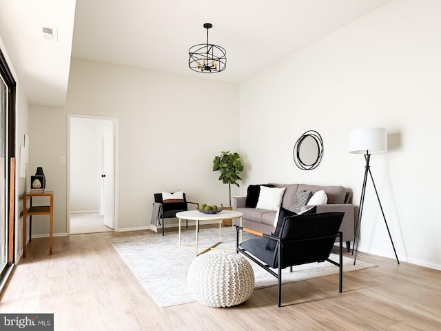 living area with baseboards, a notable chandelier, visible vents, and light wood-style floors