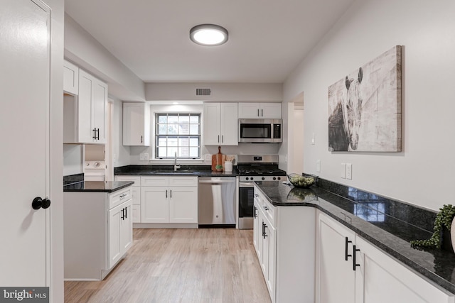 kitchen with stainless steel appliances, light wood finished floors, a sink, and white cabinetry