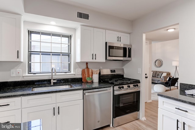 kitchen with visible vents, appliances with stainless steel finishes, white cabinets, a sink, and dark stone counters