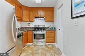 kitchen featuring stainless steel appliances, brown cabinetry, and under cabinet range hood