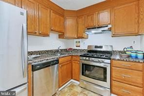 kitchen featuring stainless steel appliances, brown cabinetry, and under cabinet range hood