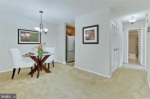 dining area featuring light colored carpet, a notable chandelier, and baseboards