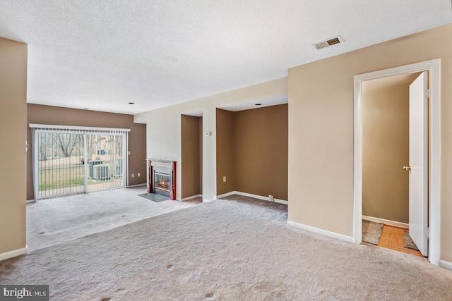 unfurnished living room with visible vents, baseboards, a fireplace with flush hearth, carpet, and a textured ceiling