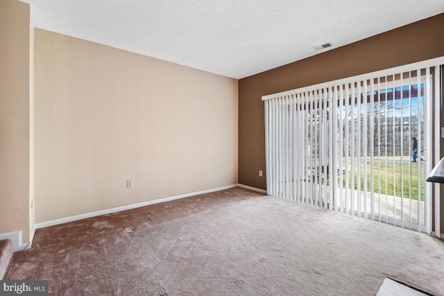 spare room featuring carpet floors, visible vents, a textured ceiling, and baseboards