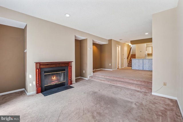 unfurnished living room featuring recessed lighting, carpet flooring, a fireplace with flush hearth, baseboards, and stairway