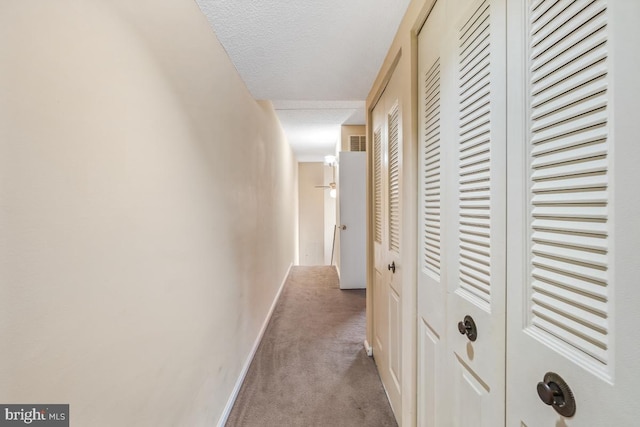 corridor with a textured ceiling, carpet floors, visible vents, and baseboards