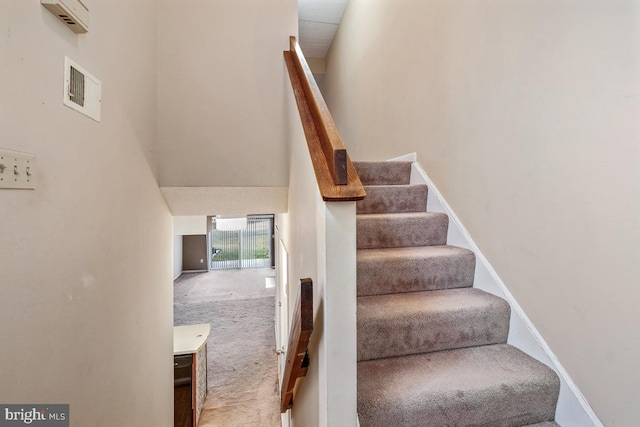 staircase featuring a high ceiling, carpet, visible vents, and baseboards