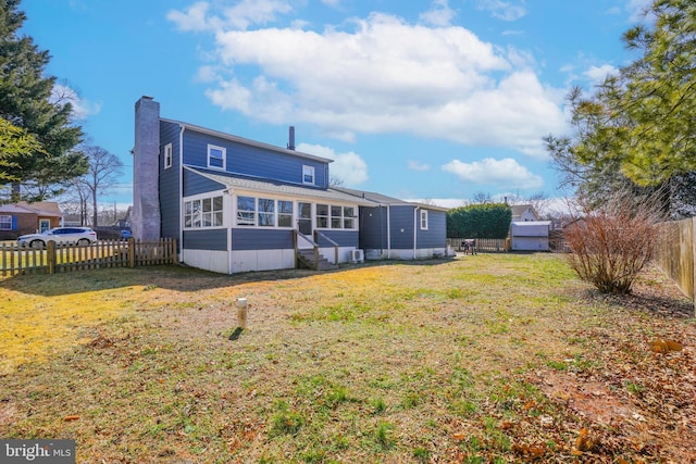 back of property with a chimney, a lawn, entry steps, a sunroom, and a fenced backyard