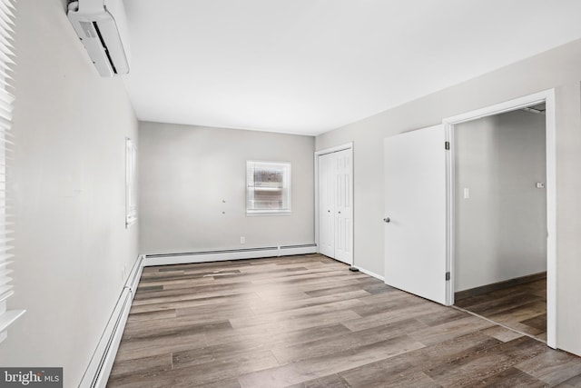 unfurnished bedroom featuring a baseboard heating unit, a closet, a wall mounted AC, and wood finished floors