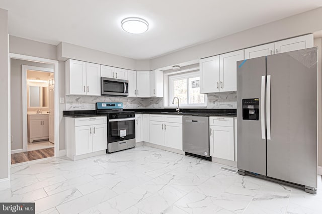 kitchen with marble finish floor, dark countertops, appliances with stainless steel finishes, white cabinetry, and a sink