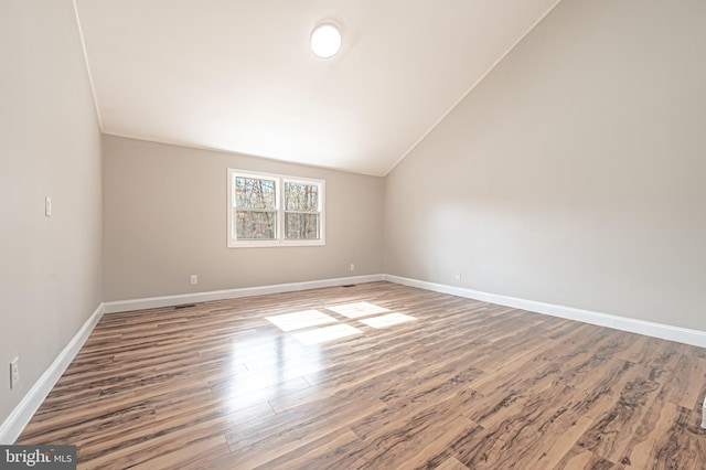 spare room featuring baseboards, vaulted ceiling, and wood finished floors