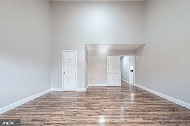 spare room with a towering ceiling, baseboards, and wood finished floors