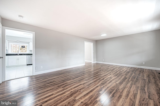 empty room with dark wood-type flooring, a sink, and baseboards