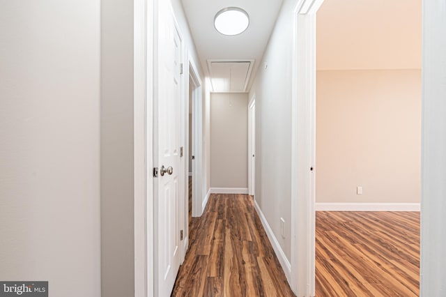 hallway featuring wood finished floors, attic access, and baseboards