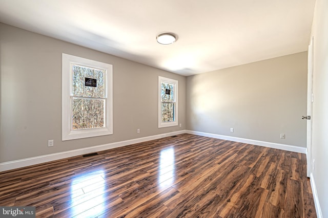 spare room featuring dark wood-style flooring, visible vents, and baseboards