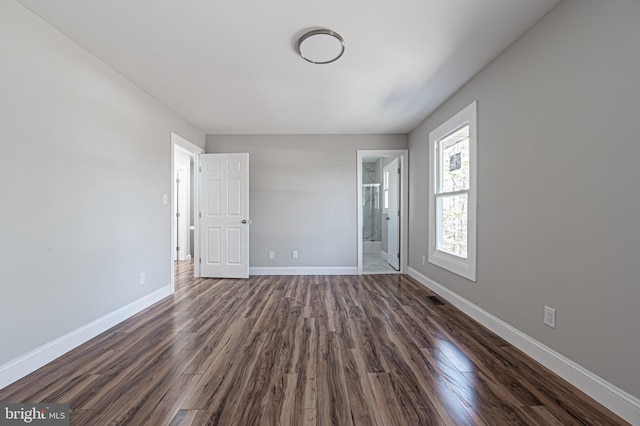 unfurnished bedroom featuring ensuite bathroom, dark wood-style flooring, visible vents, and baseboards