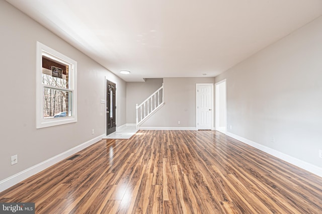 empty room featuring wood finished floors, visible vents, baseboards, and stairs