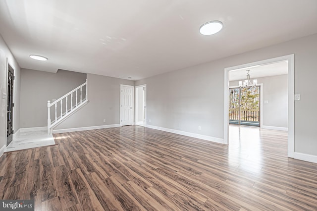 unfurnished living room with baseboards, stairway, wood finished floors, and a notable chandelier