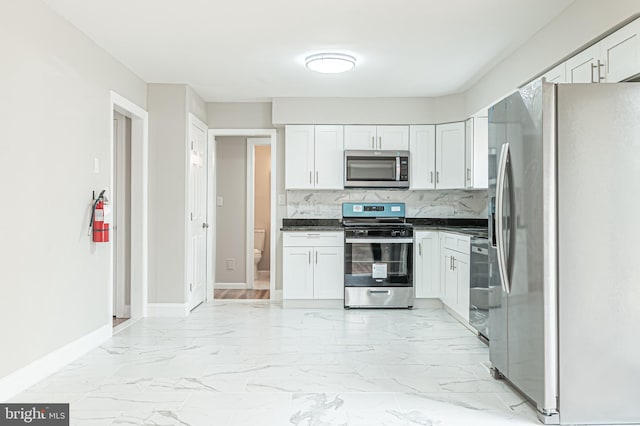 kitchen with marble finish floor, dark countertops, backsplash, appliances with stainless steel finishes, and white cabinetry