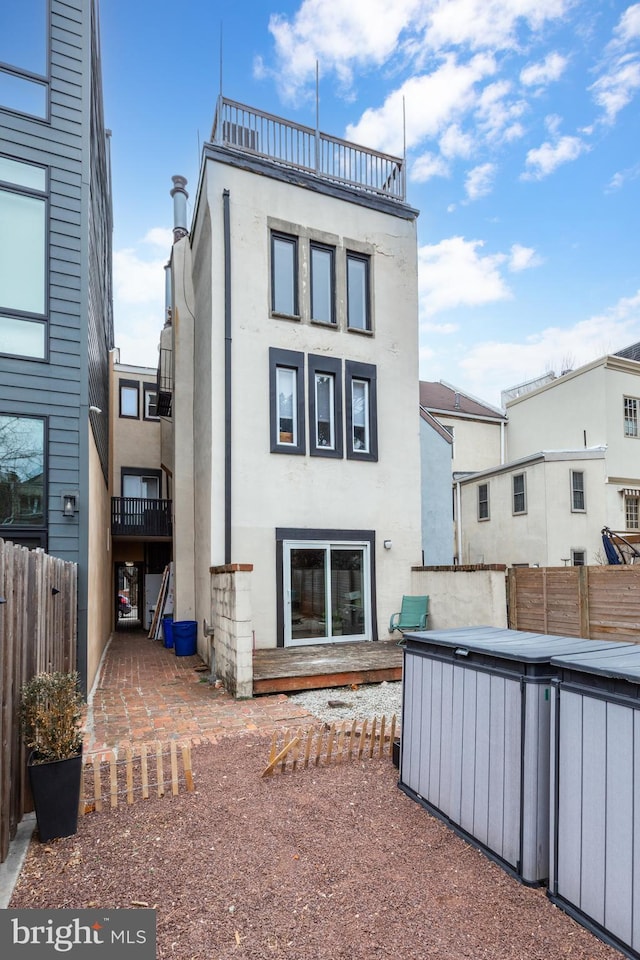 back of property with stucco siding, a jacuzzi, a balcony, and fence