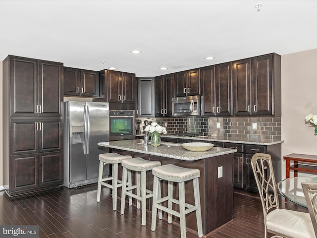 kitchen featuring an island with sink, a kitchen breakfast bar, tasteful backsplash, dark wood finished floors, and appliances with stainless steel finishes