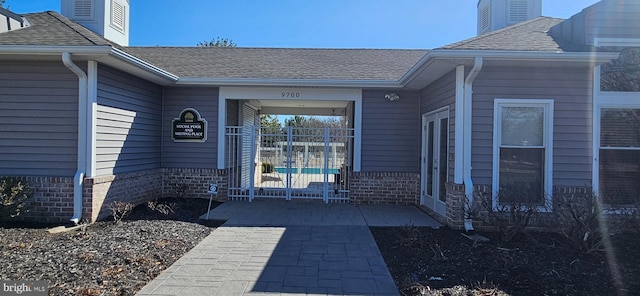 property entrance with brick siding, roof with shingles, a chimney, and fence