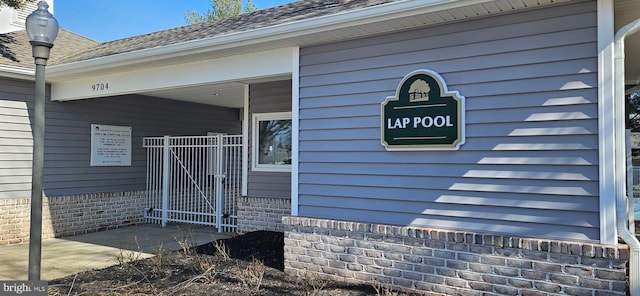 doorway to property featuring brick siding and roof with shingles