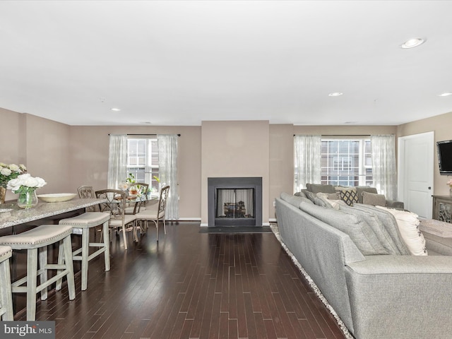 living area with recessed lighting, a fireplace with flush hearth, and dark wood-type flooring