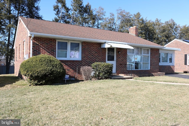 ranch-style house featuring brick siding, a chimney, a front yard, and a shingled roof