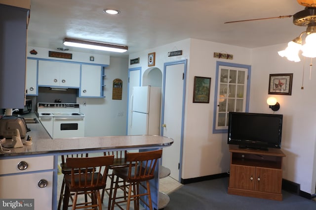 kitchen with a breakfast bar, white appliances, a peninsula, white cabinets, and baseboards