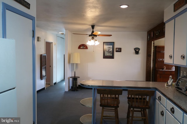 kitchen with dark countertops, ceiling fan, a breakfast bar area, a peninsula, and freestanding refrigerator