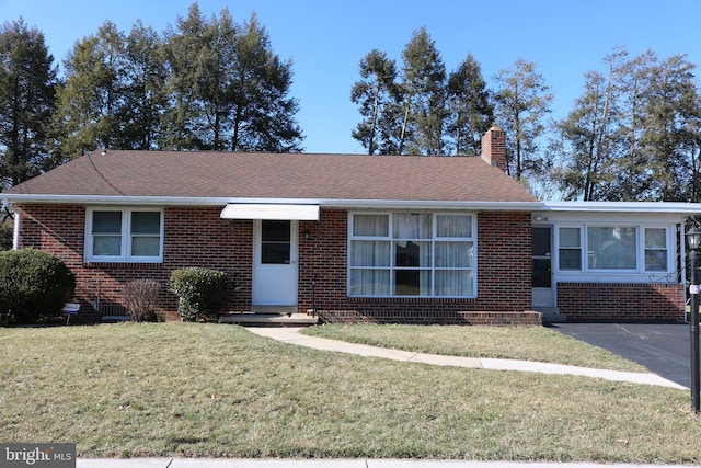 ranch-style home featuring brick siding, a chimney, a front lawn, and a shingled roof