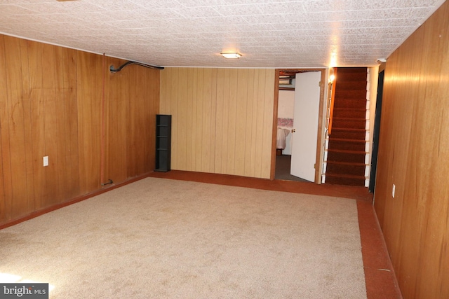 unfurnished room featuring wooden walls, stairs, and carpet