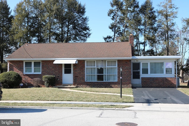 ranch-style home with a shingled roof, a front yard, brick siding, and a chimney