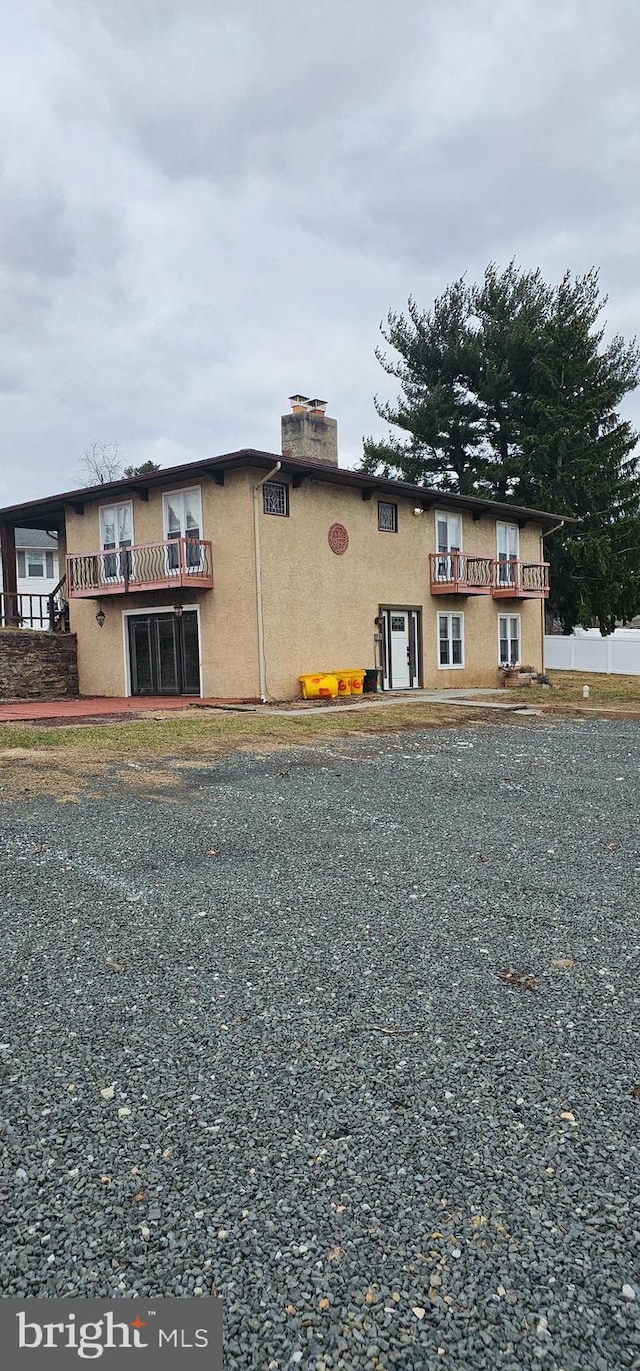 view of front of home featuring a balcony, a chimney, and stucco siding