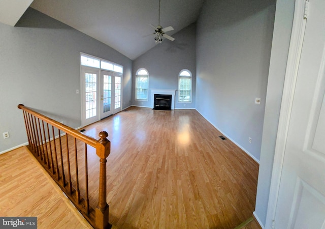 unfurnished living room with a ceiling fan, french doors, wood finished floors, and a glass covered fireplace