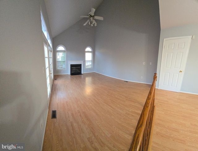 unfurnished living room featuring visible vents, light wood-style flooring, a glass covered fireplace, ceiling fan, and high vaulted ceiling