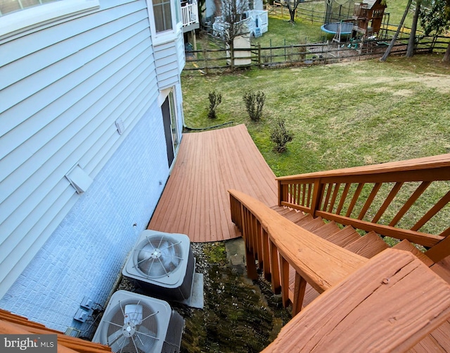 wooden terrace with a trampoline, cooling unit, a lawn, and fence