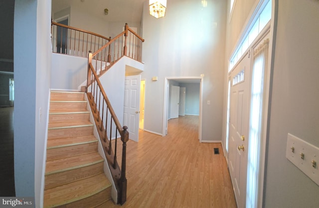 foyer entrance featuring wood finished floors, visible vents, a towering ceiling, stairs, and baseboards