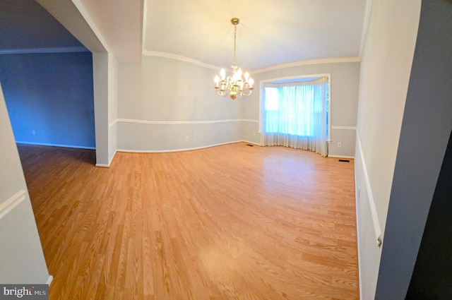 spare room featuring baseboards, ornamental molding, a chandelier, and wood finished floors