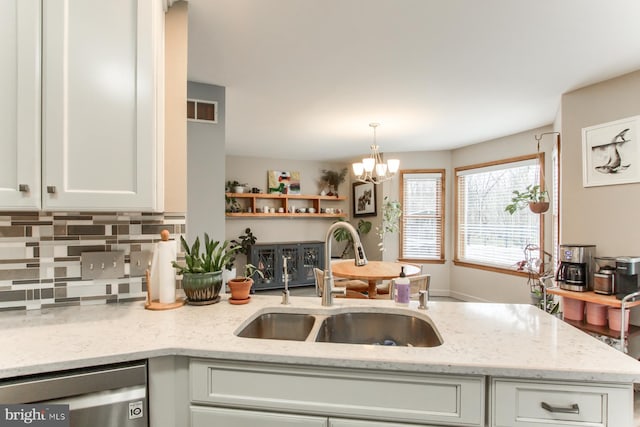 kitchen with a chandelier, light stone counters, stainless steel dishwasher, white cabinets, and a sink