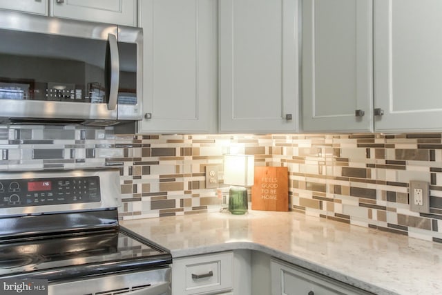 kitchen with light stone counters, stainless steel appliances, white cabinets, and decorative backsplash