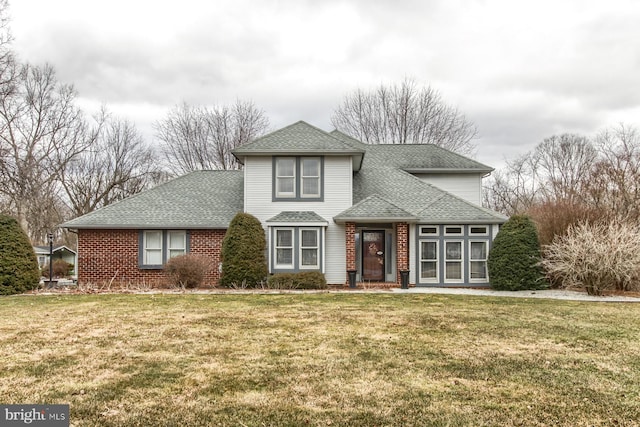 traditional-style house with brick siding, a front yard, and roof with shingles