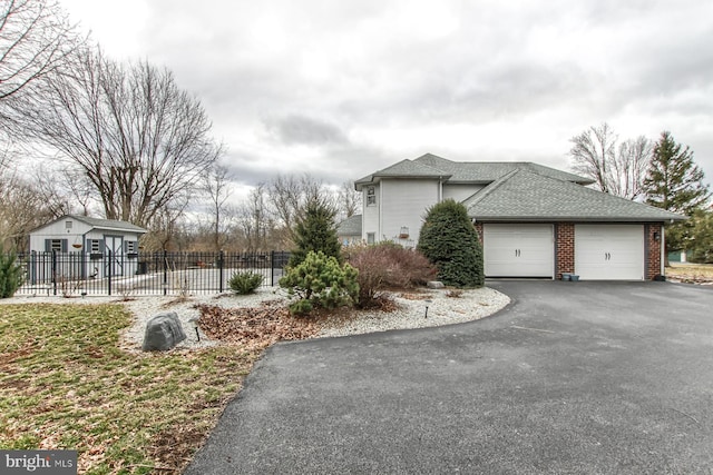 view of side of property featuring driveway, fence, a shingled roof, a garage, and brick siding