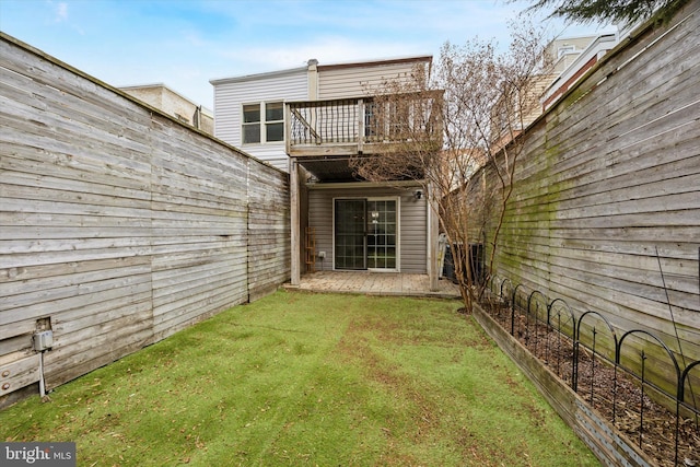 rear view of house with a fenced backyard, a yard, and a balcony