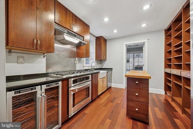 kitchen featuring beverage cooler, appliances with stainless steel finishes, dark wood-type flooring, under cabinet range hood, and recessed lighting