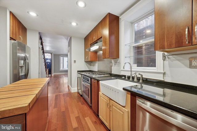 kitchen featuring butcher block counters, appliances with stainless steel finishes, dark wood-type flooring, under cabinet range hood, and a sink