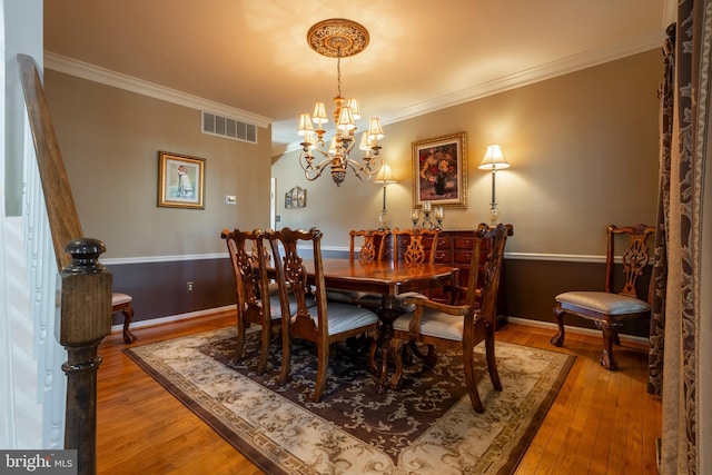 dining space featuring wood finished floors, visible vents, a chandelier, and ornamental molding