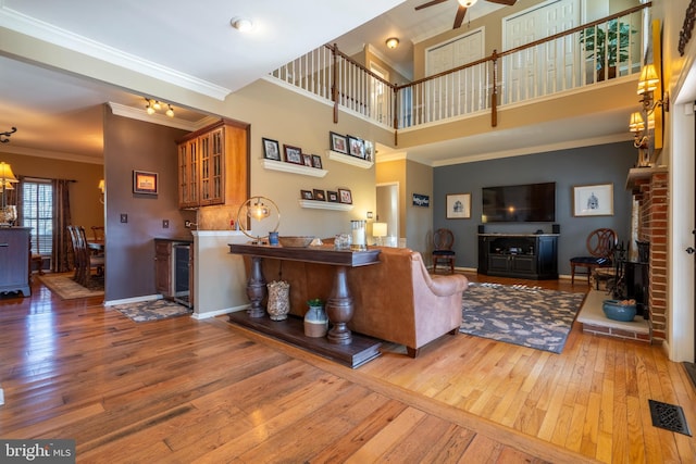 living room featuring ornamental molding, wood-type flooring, a high ceiling, baseboards, and ceiling fan